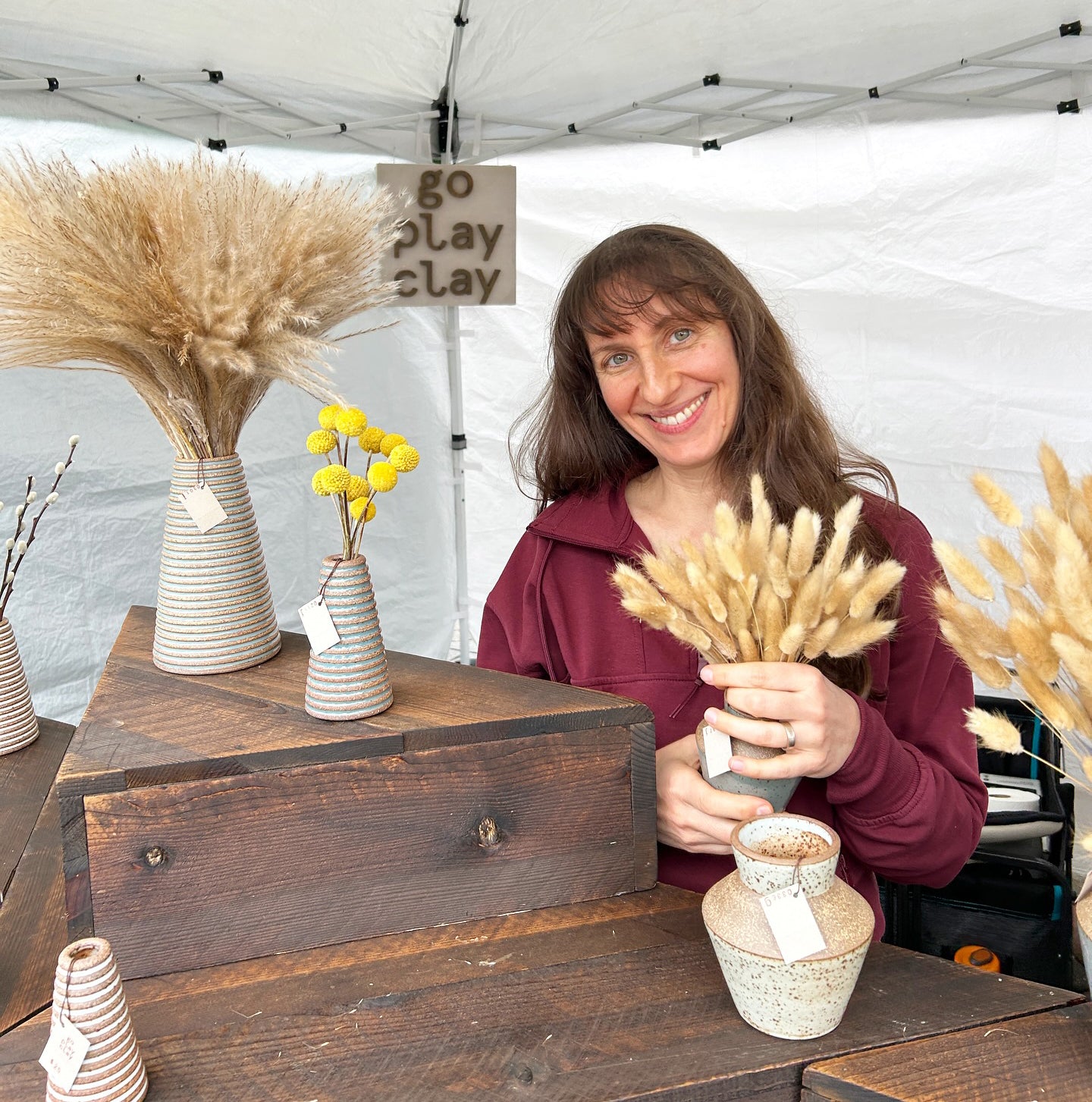 Woman at a craft fair with ceramic vases and dried plants